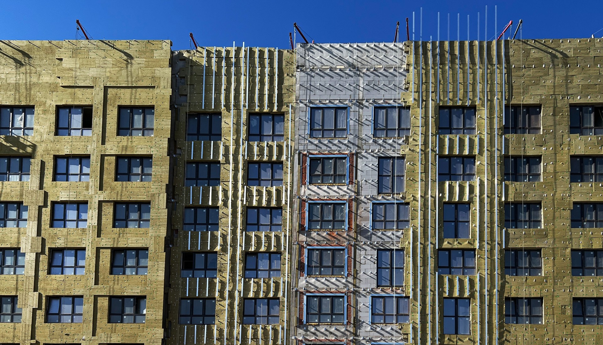 Multi-story building under renovation, showcasing exposed insulation layers and unfinished facade. The construction process is visible, steps in facade upgrade